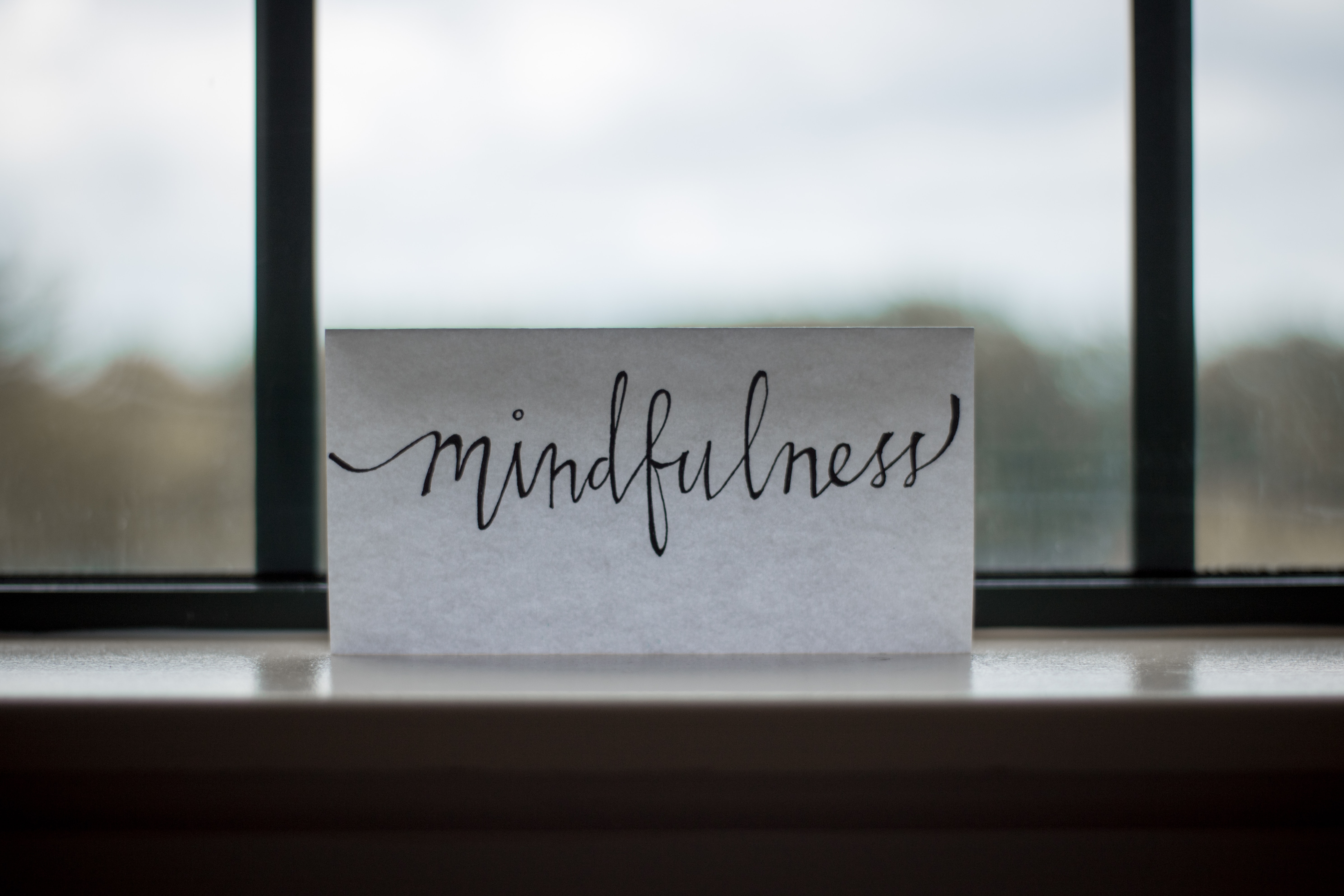 Handwritten word “mindfulness” on a card by a window.